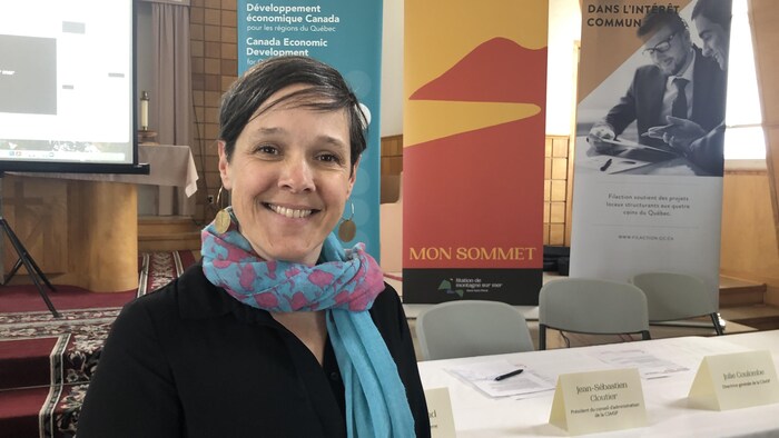 Julie Coulombe devant des affiches et une table préparée pour la conférence de presse.