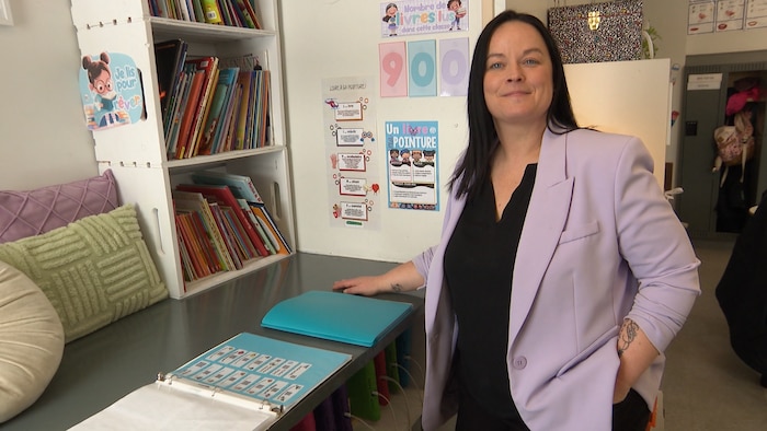 Une femme avec un veston mauve se tient debout tout près d'une table avec des livres.