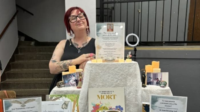 Julie Vieira est assise devant une table où sont exposés des objets sur le thème de la mort.