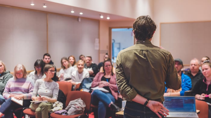Une personne de dos donne une formation à un public assis sur des chaises.