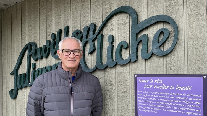 Gaétan Cliche devant le Pavillon Julienne-Cliche et l'affiche apposée à côté.