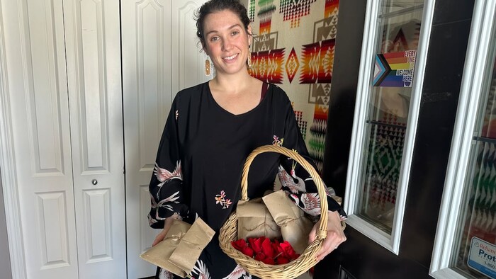 Une femme souriante tient un panier d'osier contenant des paquets et des emballages rouges.