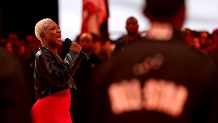 La chanteuse Jully Black porte un veston de cuir noir et une jupe rouge alors qu'elle chante l'hymne national canadien.