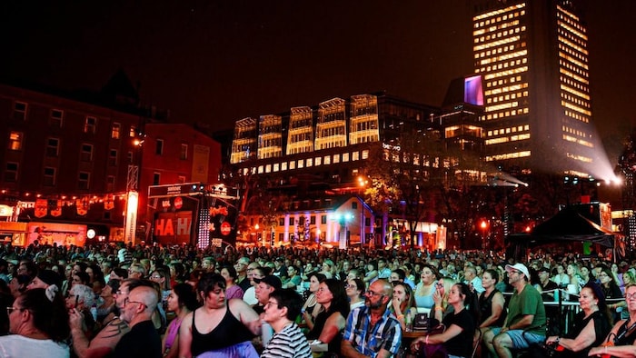 Photographie nocturne montrant une foule dense assise à la Place George-V à Québec lors d'un festival d'humour en plein air.