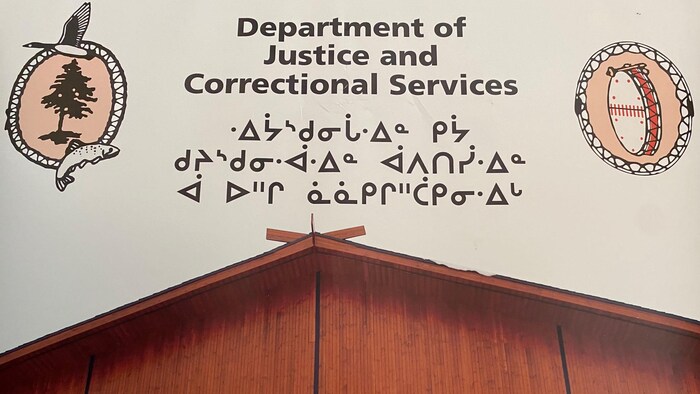 Une affiche avec un bâtiment, un tambour, un arbre entouré d'un poisson et d'une outarde et l'inscription en anglais et cri : département de la justice et des services correctionnels.