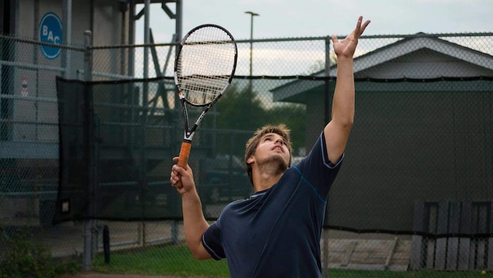 Justine Bourassa sur un terrain de tennis faisant un service.