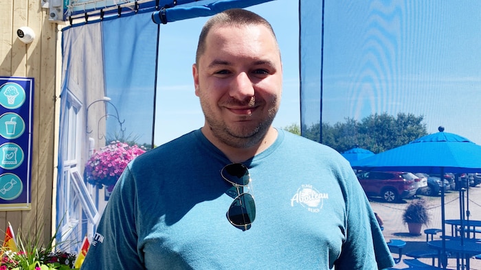 Un homme en t-shirt bleu est dehors en plein soleil et il sourit.