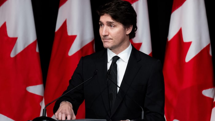 Le premier ministre Justin Trudeau fait un discours, l'air dépité, devant des drapeaux canadiens.