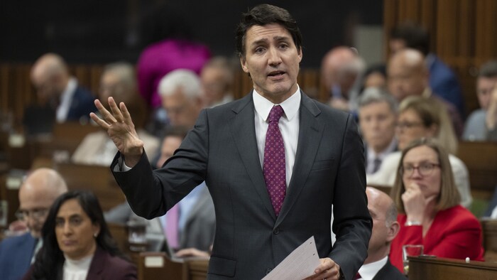 Justin Trudeau debout à la Chambre des communes. Il parle et tient une feuille dans sa main gauche. 