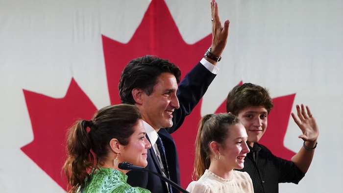 Justin Trudeau, Sophie Grégoire Trudeau et leurs enfants Xavier et Ella-Grace saluent une foule devant une immense feuille d'érable sur un drapeau du Canada.