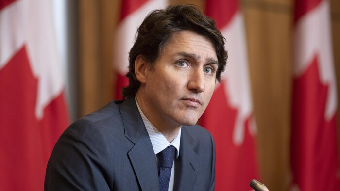 رئيس الحكومة الكندية جوستان ترودو في مؤتمر صحفي وتبدو خلفه أعلام كندية.