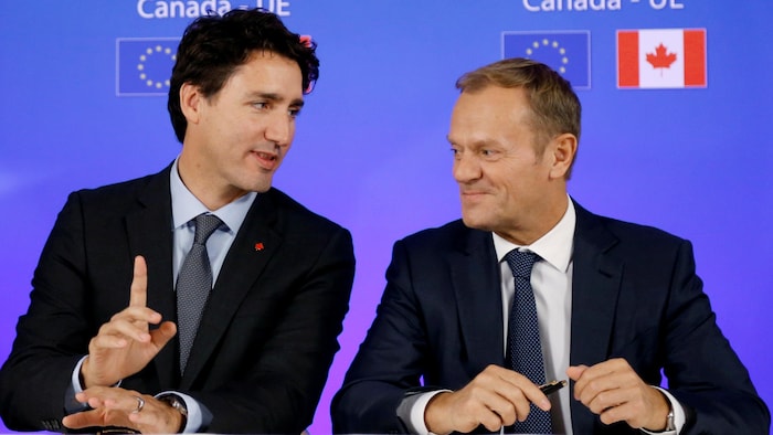 Justin Trudeau and Donald Tusk look at each other to sign a deal.