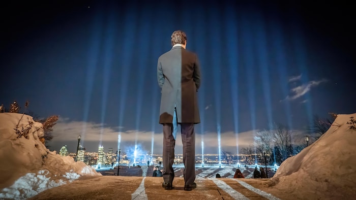 Justin Trudeau vu de dos, devant 14 faisceaux de lumière montant vers le ciel.