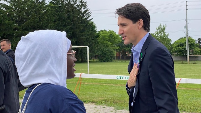 رئيس الحكومة الكندية جوستان ترودو متحدثاً إلى امرأة سوداء البشرة تضع حجاب رأس أبيض اللون.