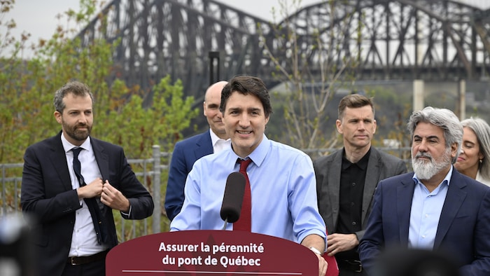 Justin Trudeau en conférence de presse avec le pont de Québec en arrière-plan.