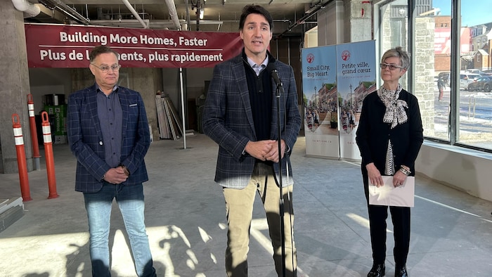 Justin Trudeau en conférence de presse avec Donna Reardon et Wayne Long dans un immeuble en construction. 