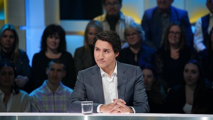 Un homme écoute une question dans un décor de télévision.