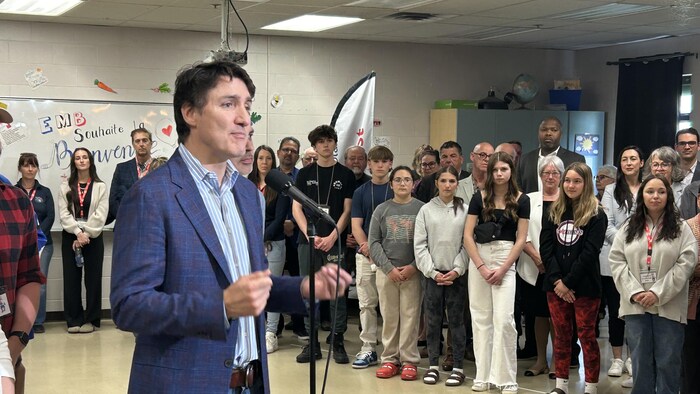 Justin Trudeau dans une salle de classe avec des élèves derrière lui. 