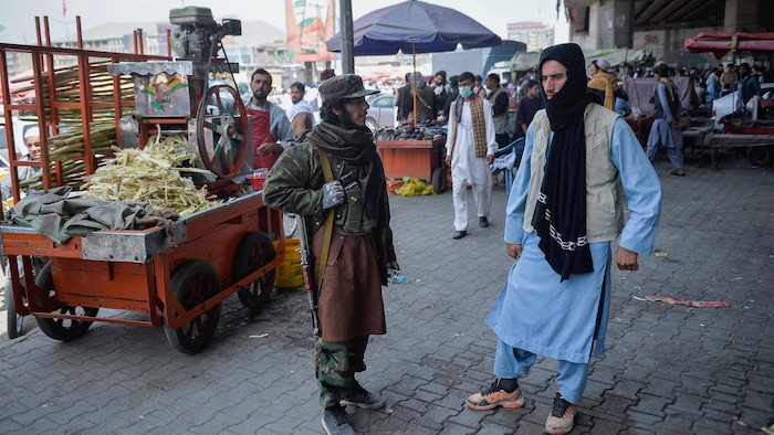 Un taliban armé discute avec un autre homme sur une place publique. 