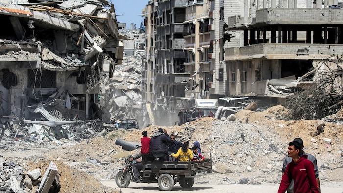 Hommes, femmes et enfants se déplacent dans un véhicule à trois roues au milieu des décombres d'immeubles.
