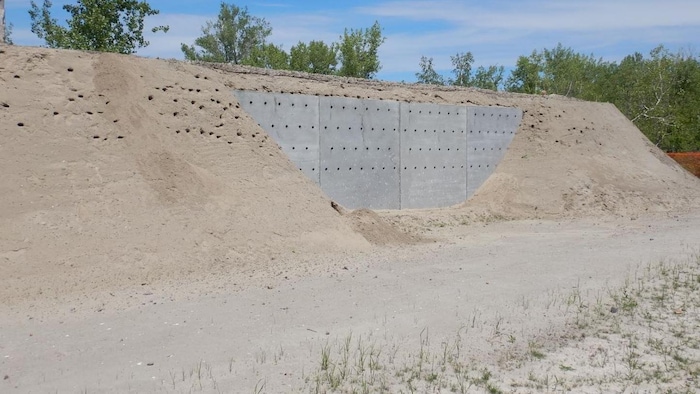 Un énorme talus de sable soutient une paroi de béton avec des trous pré-creusés.