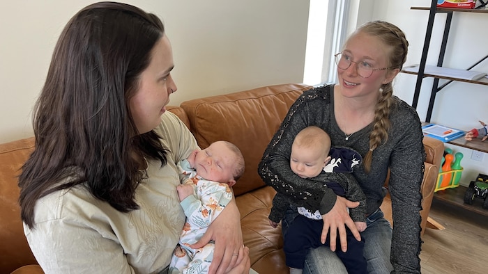 Sabrina et Kaïla Boivin sont assises sur un divan et discutent, leur bébé dans les bras.