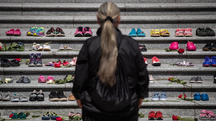 Une femme, de dos, regardant les chaussures d'enfants alignées sur des marches.