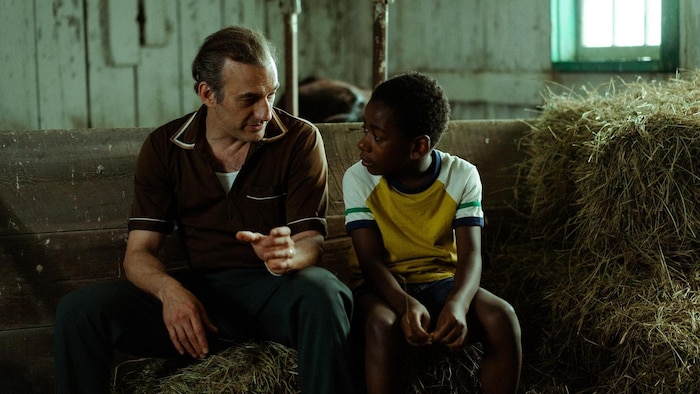 Un homme et un jeune garçon sont assis sur une botte de foin dans une étable. 