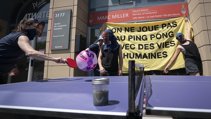 Des militants jouent au ping-pong symboliquement avec des masques de ministres. Au premier plan, un échantillon d'eau plutôt grise.
