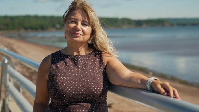 Une femme souriante debout sur une passerelle, au bord de la mer.