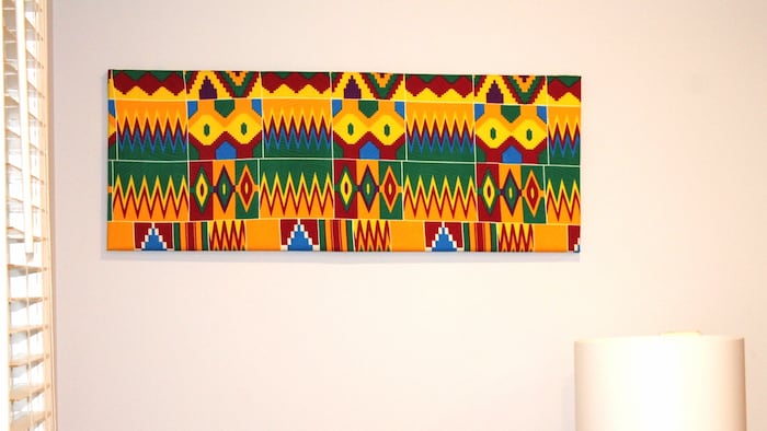 Une œuvre d'art confectionnée avec des pagnes africains accrochée à un mur blanc