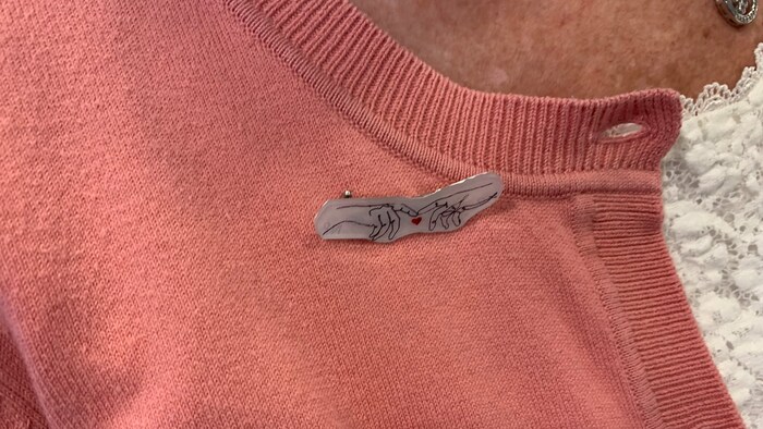 Isang pin na may disenyo ng dalawang kamay na may hawak na puso.
