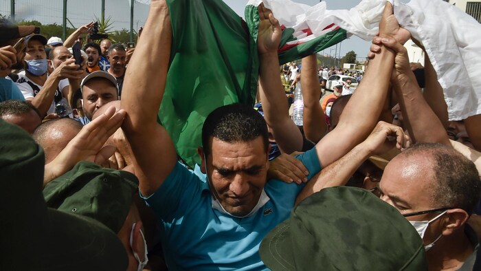Il est au milieu d'une foule portant le drapeau algérien.