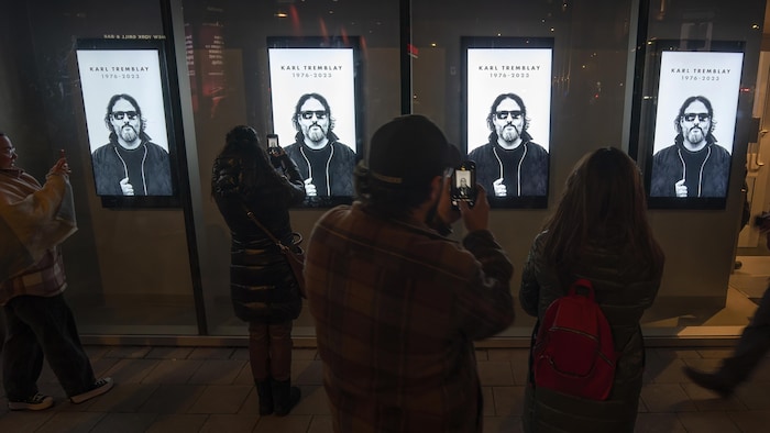 Quelques personnes prennent en photo quatre affiches montrant le chanteur Karl Tremblay. 