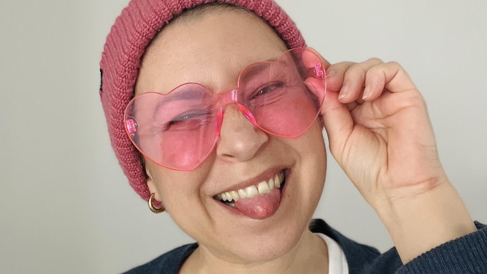Une femme avec des lunettes roses sourit en tirant la langue.