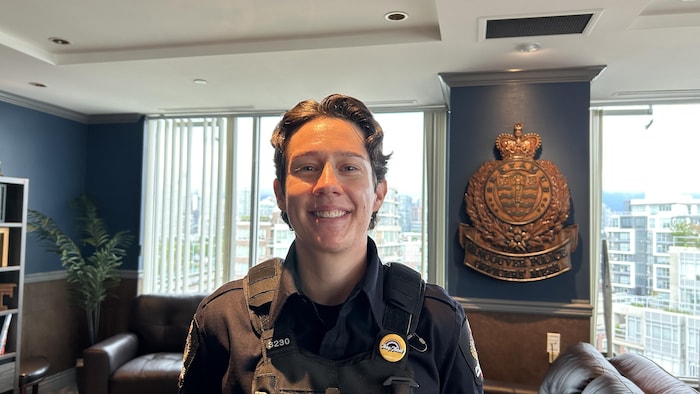 Kat Dauncey sourit à la caméra. Elle porte un uniforme avec une pinne avec petit drapeau de la fierté dessus.