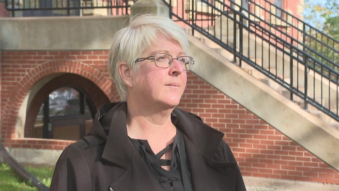 Kate MacQuarrie devant les marches d'un édifice regarde au loin.