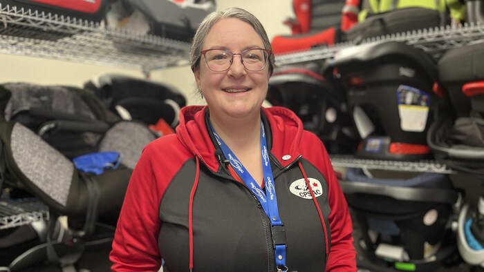 Une femme sourit pour la caméra, devant des tablettes sur lesquelles se trouvent des sièges d'auto pour enfants.
