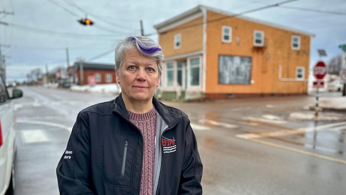 Kathleen Couture est debout dans une rue et pose pour une photo. Un bâtiment jaune apparaît de l'autre côté de la rue.