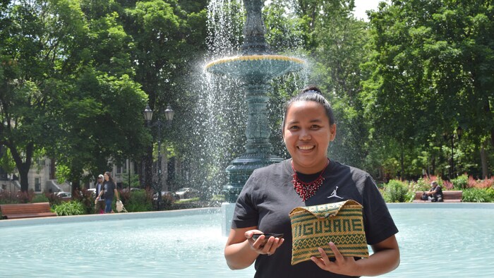 Une femme se tient debout devant une fontaine avec des objets traditionnels dans les mains.