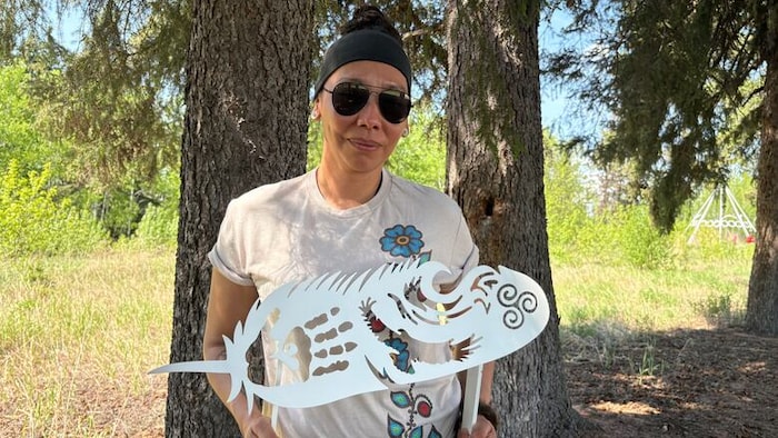 Katrina Maurice tient une pierre tombale en métal en forme de plume à l'intérieur de laquelle une main et un aigle ont été gravés.