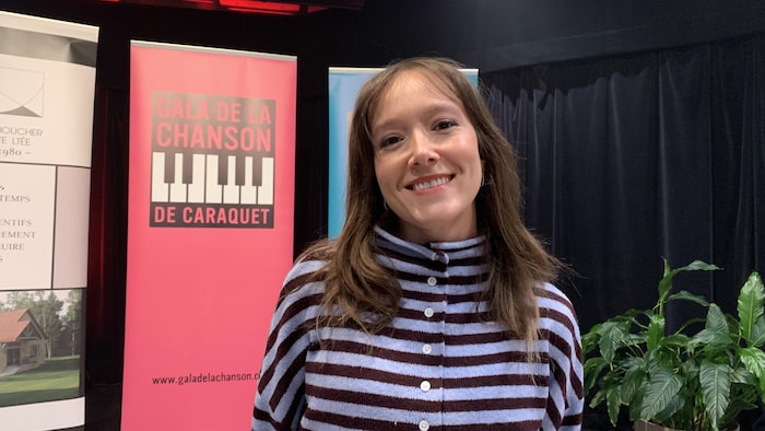 Une femme souriante devant la bannière du Gala de la chanson de Caraquet. 