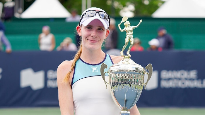Kayla Cross sourit en tenant le trophée des Championnats Banque Nationale de Granby sur un court de tennis.
