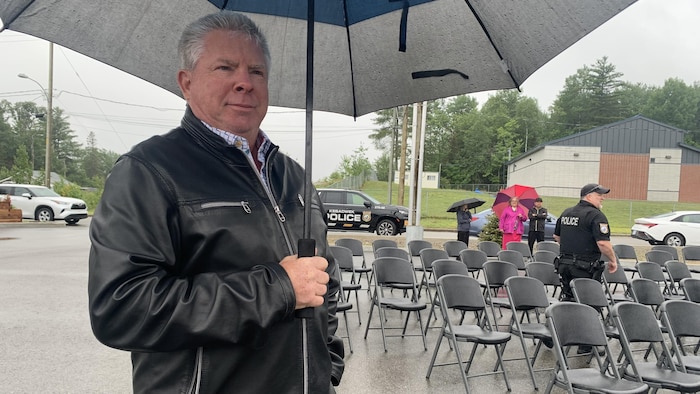 Martin Lefebvre est à l'extérieur devant le poste de police avec un parapluie.