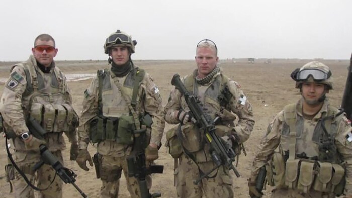Quatre soldats posent en tenue de combat dans un terrain désertique.