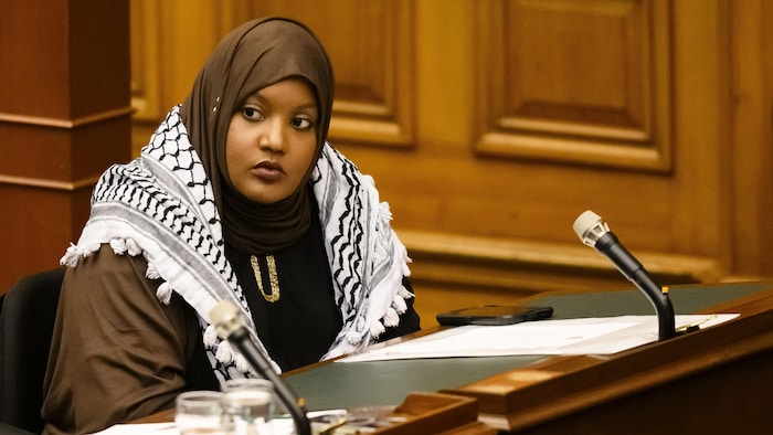 Sarah Jama dans la Chambre de l'Assemblée législative de l'Ontario et avec un keffieh palestinien sur les épaules.