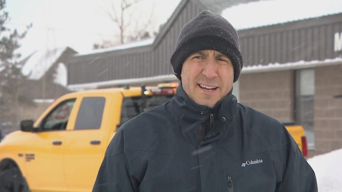 Keith Chiasson dehors sous la neige, coiffé d'une tuque et près d'une camionnette jaune.