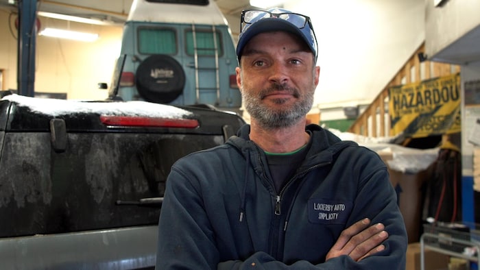 Portrait Keith Flinn dans son garage portant une casquette et des lunettes par dessus.