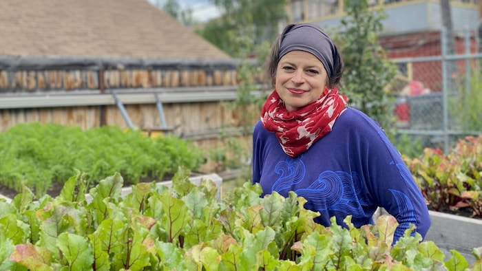 Keitha Clark sourit dans le jardin communautaire de son organisme, entourée de légumes.