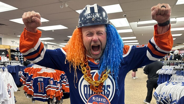 Un homme portant des produits à l'image des Oilers lève les bras en l'air pour célébrer.